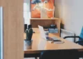 Scrivania in legno con computer portatile, tazza, smartphone e cactus in vaso in un ufficio con sedia blu e scaffale