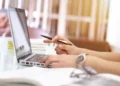Mani al lavoro su un portatile con una penna, accanto a libri e fogli: scrivania di uno studio, tema incentivi alle imprese