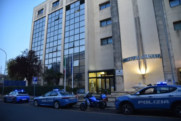 Ingresso della Questura di Ragusa al tramonto, con tre auto e una moto della Polizia di Stato a lampeggianti accesi