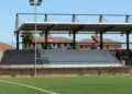 Tribuna coperta con struttura in acciaio e gradinate grigie davanti a un campo da calcio in erba sintetica a Ragusa, impianto sportivo