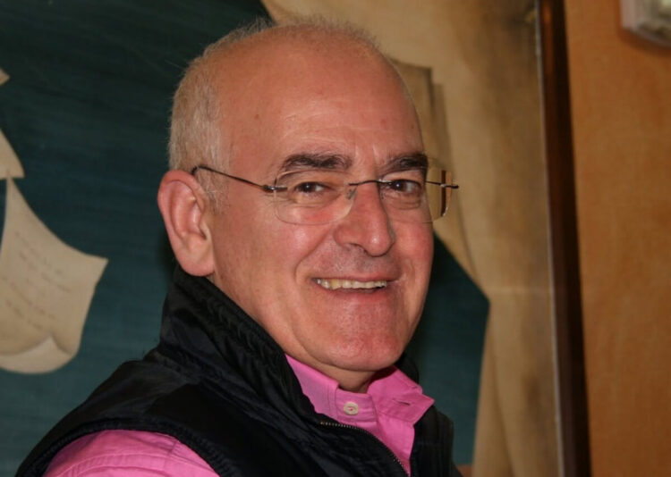 Salvatore Saccone sorridente, con occhiali senza montatura, camicia rosa e gilet nero