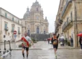 Due runner con pettorale corrono la maratona di Ragusa in piazza Duomo a Ibla, sotto la pioggia, con San Giorgio sullo sfondo
