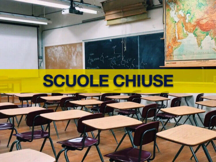 Aula scolastica vuota con banchi, sedie, lavagna e carta geografica, attraversata da una fascia gialla con la scritta «Scuole chiuse»