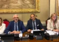 Quattro persone sedute a un banco con microfoni e documenti, in un’aula dove si discute di aiuti alle imprese siciliane