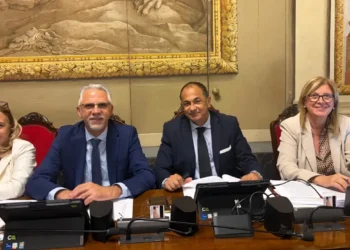 Quattro persone sedute a un banco con microfoni e documenti, in un’aula dove si discute di aiuti alle imprese siciliane