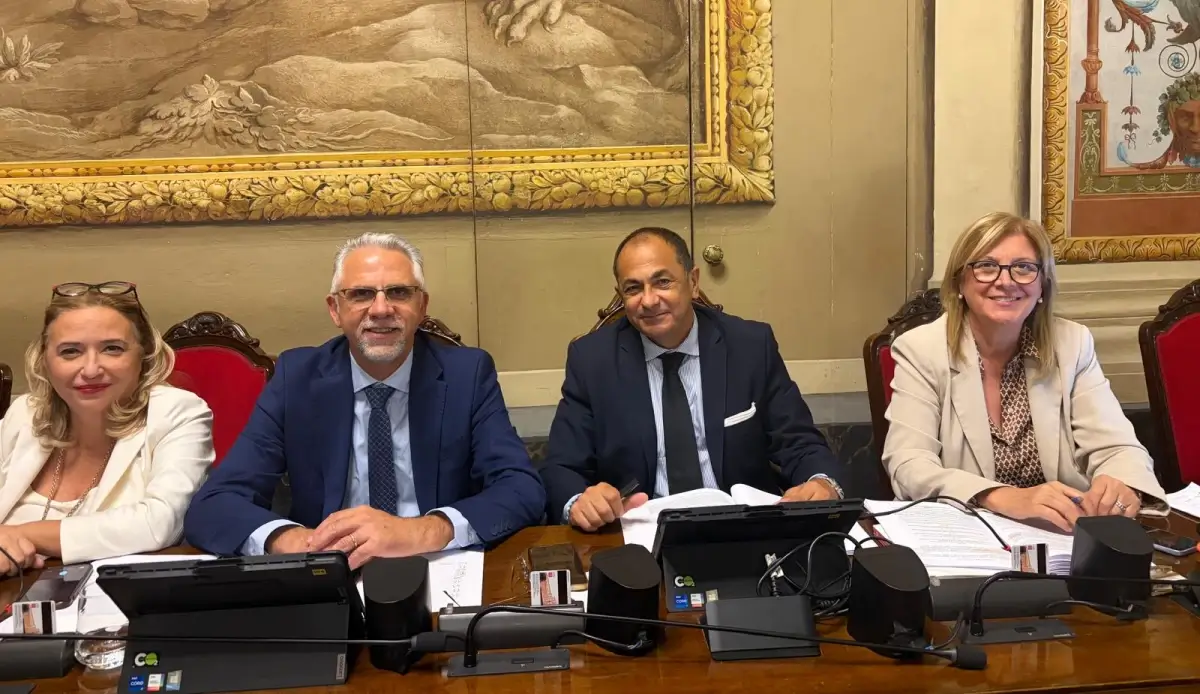 Quattro persone sedute a un banco con microfoni e documenti, in un’aula dove si discute di aiuti alle imprese siciliane