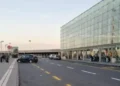 Esterno del terminal dell’aeroporto di Catania con auto sulla corsia e passeggeri con valigie sul marciapiede