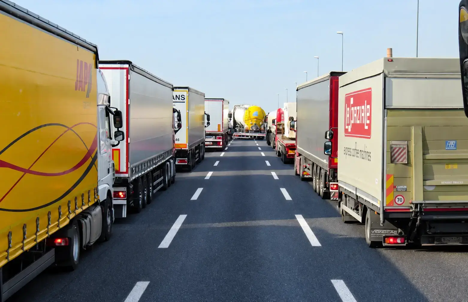 Mezzi dell’autotrasporto incolonnati su due file lungo un’autostrada a più corsie, con la carreggiata centrale sgombra