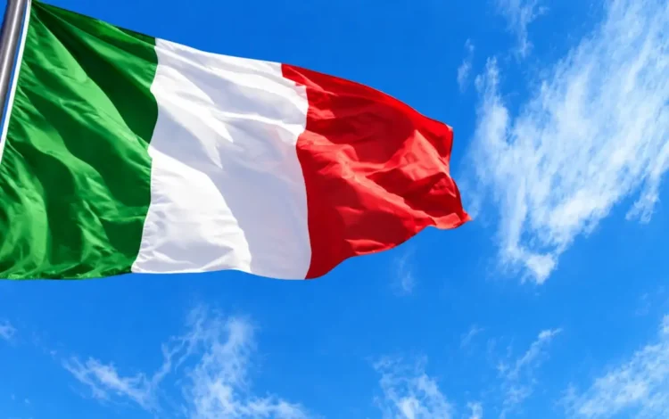 Bandiera tricolore italiana che sventola contro un cielo azzurro con nuvole sottili, simbolo del 4 novembre
