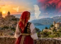 Donna in costume tradizionale guarda un borgo in Sicilia e la costa albanese. Immagine generata con intelligenza artificiale