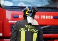 Vigile del fuoco di spalle con casco e giacca con la scritta «Vigili del Fuoco» davanti a un camion rosso dei pompieri