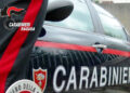 Fiancata di un’auto dei carabinieri con la banda rossa e la divisa di un militare; in alto il logo Carabinieri Ragusa
