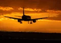 Aereo di linea in avvicinamento alla pista di un aeroporto al tramonto, in controluce contro un cielo arancione con nuvole