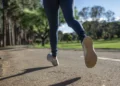 Gambe di una persona in leggings blu e scarpe da ginnastica che corre su un viale asfaltato in un parco alberato
