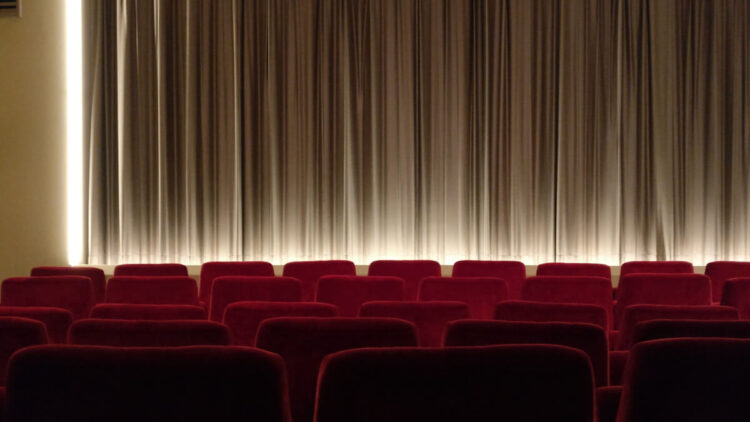 Sala di cinema con poltrone rosse e pubblico prima della proiezione