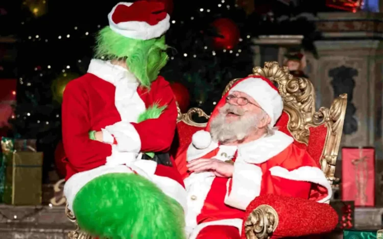 Antonino Aggius Vella vestito da Babbo Natale, seduto su un trono dorato, sorride a una persona travestita da Grinch