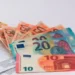 Banconote da 10, 20 e 50 euro a ventaglio accanto a una carta di pagamento e a un modulo, simbolo dell'assegno di inclusione