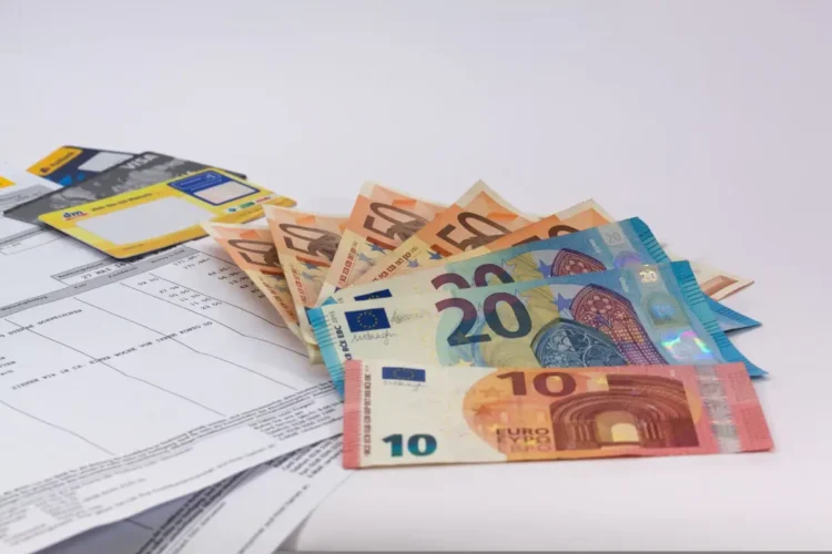 Banconote da 10, 20 e 50 euro aperte a ventaglio accanto a carte di pagamento e a un estratto conto, tema assegno unico