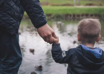 Un genitore tiene per mano un bambino di spalle davanti a uno stagno con le anatre: foto di repertorio sull'assegno unico