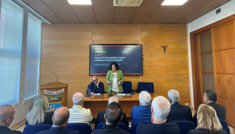 Maria Rita Schembari parla in una sala della Provincia di Ragusa; sullo schermo l’istanza di convocazione urgente