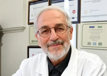 Antonio Caruso, biologo di Modica autore della ricerca Bibbia e Dna, in camice bianco davanti a una parete di attestati