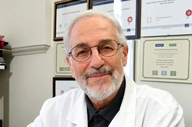 Antonio Caruso, biologo di Modica autore della ricerca Bibbia e Dna, in camice bianco davanti a una parete di attestati
