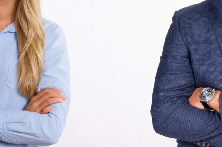 Una donna in camicia azzurra e un uomo in giacca blu, separati e a braccia conserte, ai due lati opposti dell’immagine