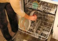Una persona carica piatti colorati e una tazza nel cestello inferiore di una lavastoviglie aperta in una cucina di casa