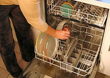 Una persona carica piatti colorati e una tazza nel cestello inferiore di una lavastoviglie aperta in una cucina di casa
