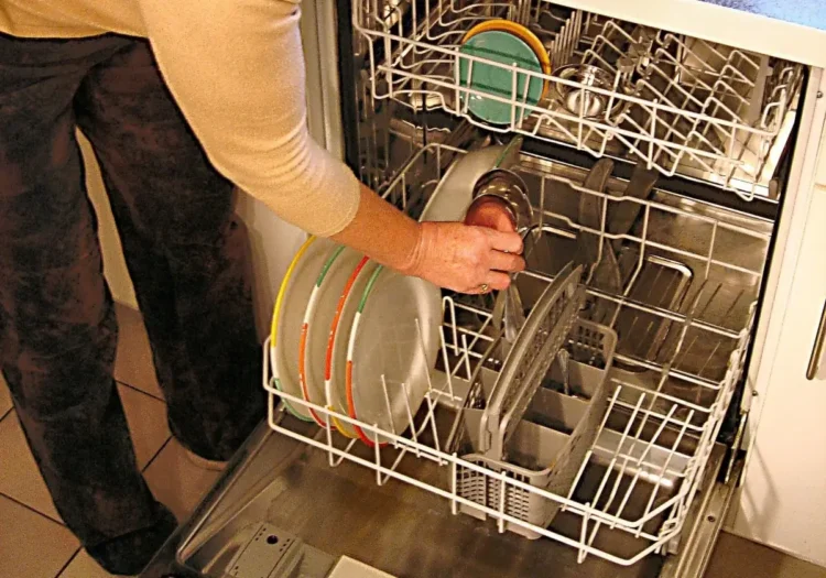 Una persona carica piatti colorati e una tazza nel cestello inferiore di una lavastoviglie aperta in una cucina di casa