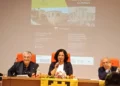Tre relatori al tavolo durante la conferenza sui Cabrera a Comiso, sotto la proiezione del programma della serata