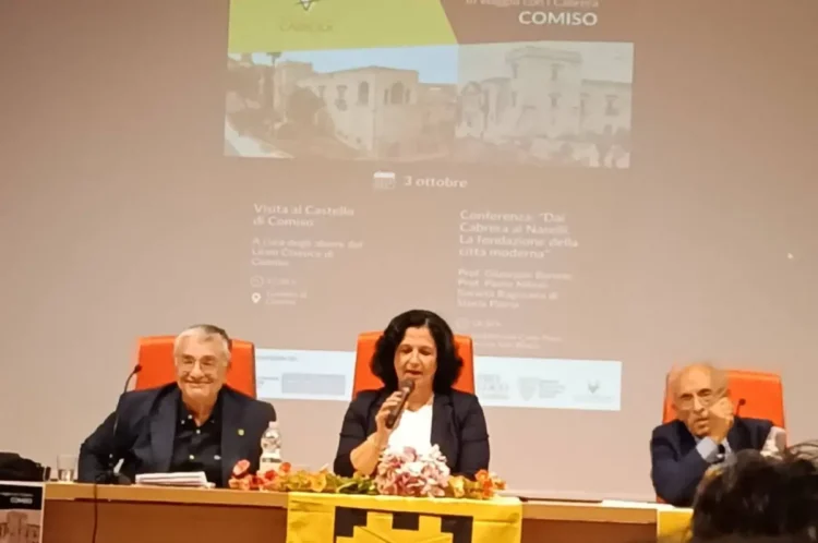 Tre relatori al tavolo durante la conferenza sui Cabrera a Comiso, sotto la proiezione del programma della serata