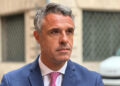 Il senatore Salvo Sallemi, che commenta il calo dei reati a Ragusa, in giacca blu e cravatta rosa davanti a un palazzo