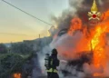 Vigile del fuoco con autorespiratore getta acqua sul camion in fiamme a bordo della SS 115, tra fichi d'india e fumo all'alba