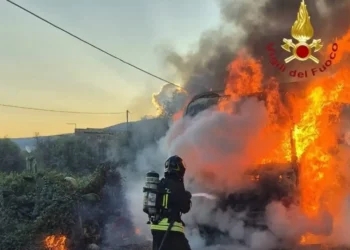Vigile del fuoco con autorespiratore getta acqua sul camion in fiamme a bordo della SS 115, tra fichi d'india e fumo all'alba