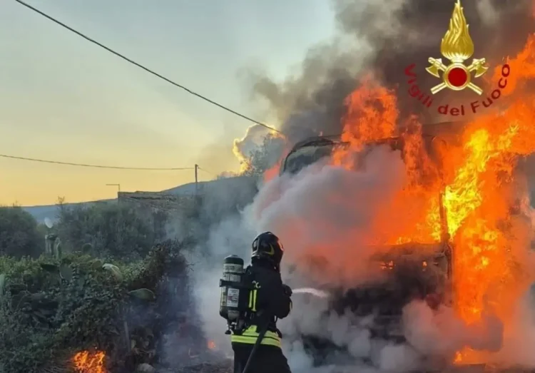 Vigile del fuoco con autorespiratore getta acqua sul camion in fiamme a bordo della SS 115, tra fichi d'india e fumo all'alba