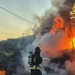 Vigile del fuoco con autorespiratore getta acqua sul camion in fiamme a bordo della SS 115, tra fichi d'india e fumo all'alba