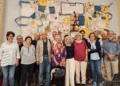 Il comitato Comiso cantiere per la pace in posa davanti a un arazzo con giubbotti di salvataggio e la scritta «Io accolgo»