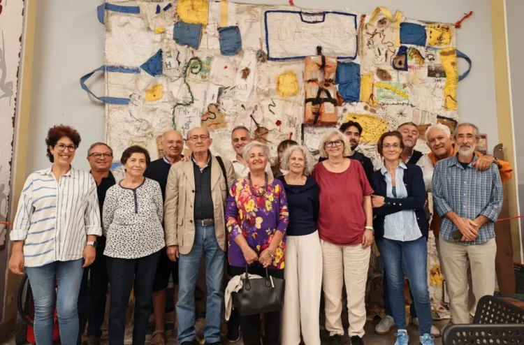 Il comitato Comiso cantiere per la pace in posa davanti a un arazzo con giubbotti di salvataggio e la scritta «Io accolgo»