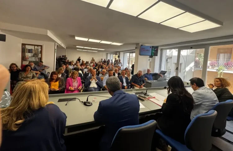 Sala piena all'incontro sul caro carburante a Ragusa: il pubblico seduto davanti al tavolo dei relatori con i microfoni
