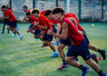 Calciatori del Frigintini con maglia rossa e pantaloncini blu scattano in fila durante un allenamento su un campo in erba sintetica