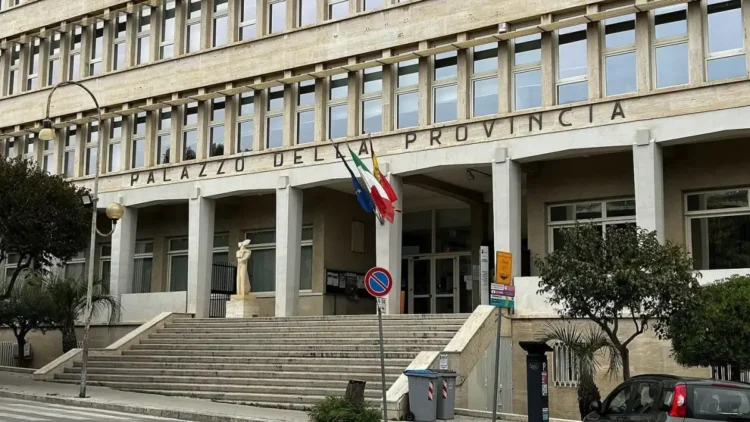 Facciata del Palazzo della Provincia di Ragusa con scalinata, colonne, bandiere e scritta in lettere metalliche sopra l'ingresso