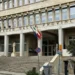 Facciata del Palazzo della Provincia di Ragusa con scalinata, colonne, bandiere e scritta in lettere metalliche sopra l'ingresso