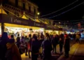 Stand di ChocoModica illuminati di sera lungo una via di Modica, con visitatori tra le bancarelle e luminarie sopra la strada