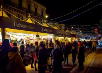 Stand di ChocoModica illuminati di sera lungo una via di Modica, con visitatori tra le bancarelle e luminarie sopra la strada