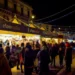 Stand di ChocoModica illuminati di sera lungo una via di Modica, con visitatori tra le bancarelle e luminarie sopra la strada