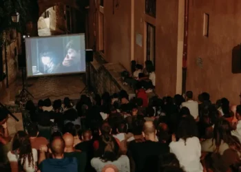 Pubblico seduto in un vicolo a gradini davanti a uno schermo all'aperto durante una serata del cinema di quartiere a Modica