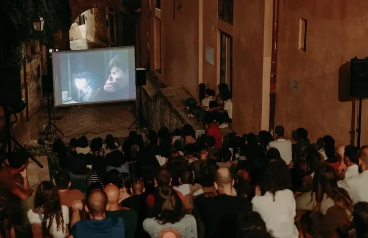 Pubblico seduto in un vicolo a gradini davanti a uno schermo all'aperto durante una serata del cinema di quartiere a Modica