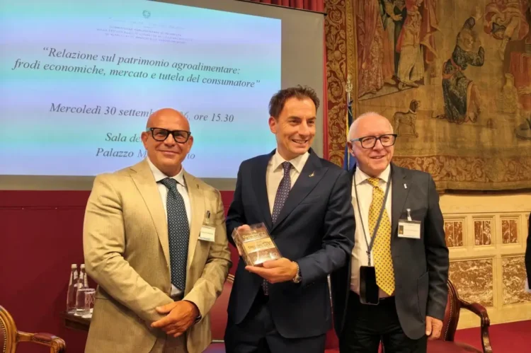 Tre uomini nella Sala della Regina di Montecitorio, quello al centro tiene una confezione di Cioccolato di Modica IGP