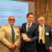 Tre uomini nella Sala della Regina di Montecitorio, quello al centro tiene una confezione di Cioccolato di Modica IGP